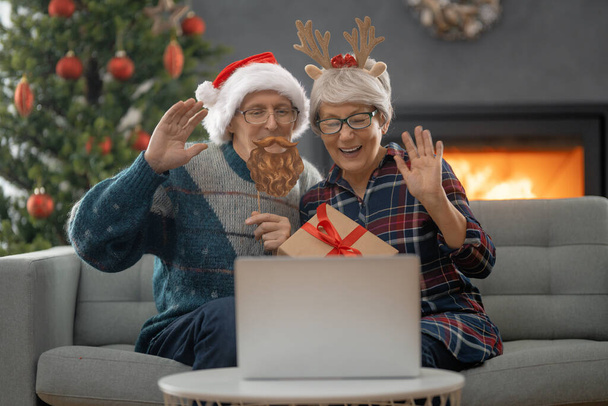 Starsza para rozmawia z kimś za pomocą laptopa w salonie urządzonym na Boże Narodzenie. - Zdjęcie, obraz