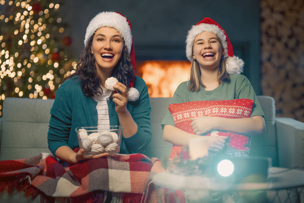 Merry Christmas and Happy New Year. People having fun near tree indoors. Loving family watching holiday movies at home. Mother and daughter spending time together. - Foto, Imagen