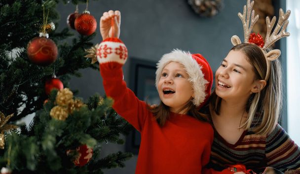 Vrolijk kerstfeest en fijne feestdagen. Vrolijke schattige kinderen meisjes thuis. Kinderen hebben plezier in de buurt van de boom in de ochtend - Foto, afbeelding