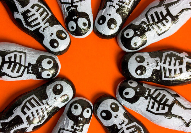Trick vagy kezelni csokoládé cukorka alakú fekete-fehér csontvázak narancssárga alapon kerek keret szöveg benne. Halloween édességek és édességek. Október 31. Vicces ijesztő karakterek. - Fotó, kép
