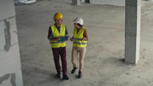 建設現場で議論し、指摘する男性と女性の白人エンジニアの高い角度ビュービデオ。8Kでレッドヘリウムカメラで撮影      - 映像、動画