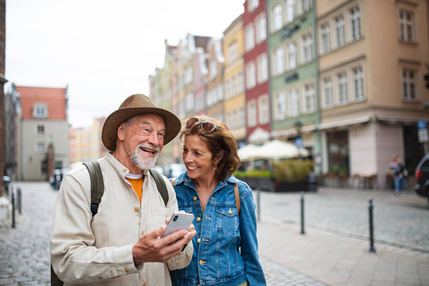 Portrait of happy senior couple tourists using smartphone outdoors in historic town - Foto, Bild