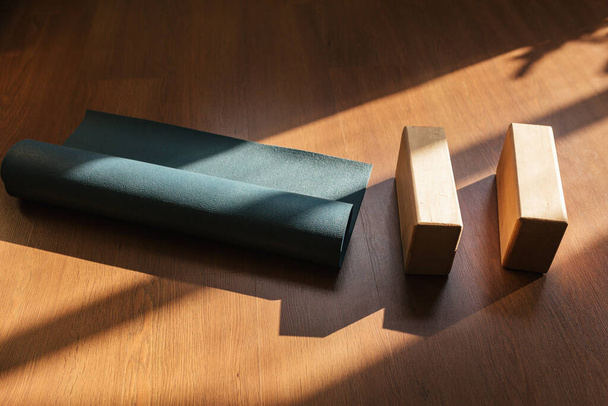 Closeup of two wooden yoga blocks and blue yoga mat on the wooden floor. - Photo, Image