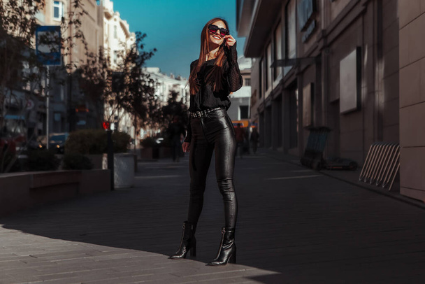 Cheerful lady in leather suit and sunglasses smiles in the street - Valokuva, kuva