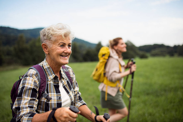 Happy mid adult woman with trekking poles hiking with active senior mother outdoors in nature. - Foto, Bild