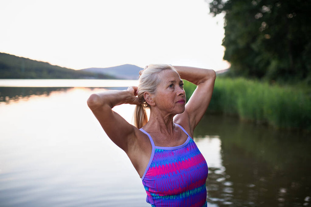 Portrait of active senior woman swimmer standing and stretching outdoors in lake. - Foto, Imagem