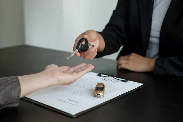 Der Autohändler berät über Kredite, Versicherungsdetails und Mietwageninformationen und liefert das Auto mit den Schlüsseln nach Unterzeichnung des Mietvertrages. - Foto, Bild
