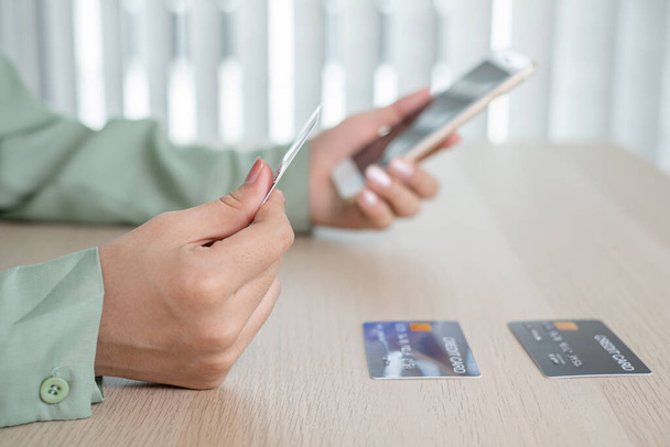 A mão da empresária está segurando um cartão de crédito e usando um smartphone para compras on-line e pagamento pela internet no escritório. - Foto, Imagem