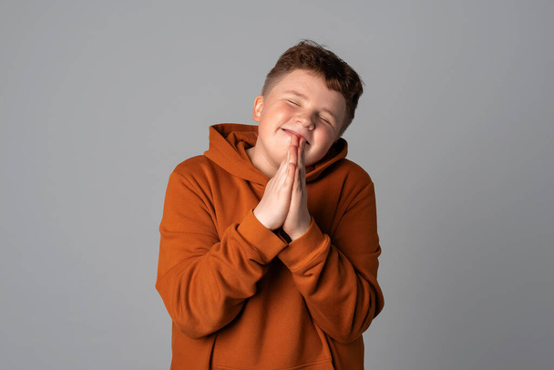 handsome teenager boy appreciate help, thanking and bowing politely with namaste gesture, pray wish beg ask luck expect, gray background - Valokuva, kuva