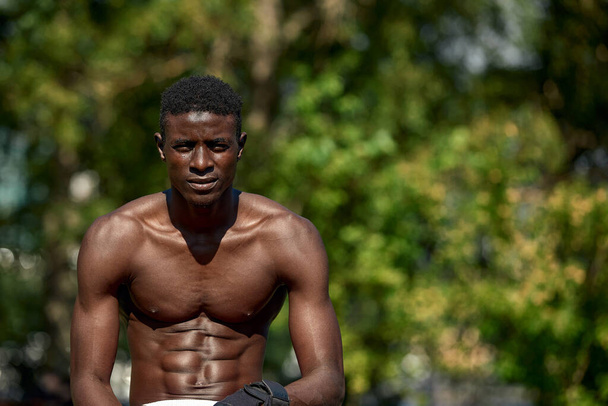 Handsome afro American runner sitting on the street while taking break after training. Black male runner having rest after workout - Photo, Image
