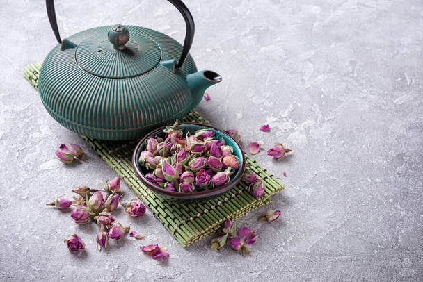 Traditional green or turquoise asian cast iron kettle with herbal tea of dried rose buds on grey concrete background - Foto, afbeelding