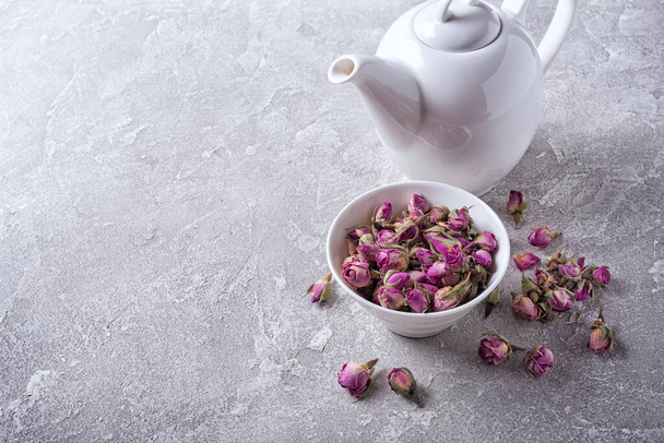 White teapot with herbal tea of dried rose buds on grey concrete background with copy space - Foto, Imagem