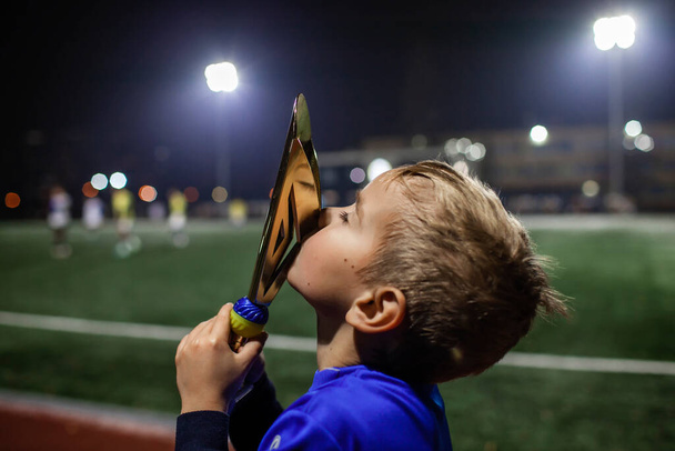 Mladý fotbalista v modrém dresu s deseti čísly drží vítěze pohár po vítězném gólu - Fotografie, Obrázek