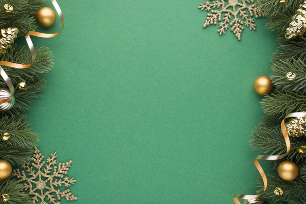 Foto von oben von Gold und Silber Weihnachtsbaumkugeln Spielzeug Kegel kleine Glöckchen Schneeflocken und Serpentin auf Kiefernzweigen auf isoliertem grünen Hintergrund mit leeren Raum - Foto, Bild