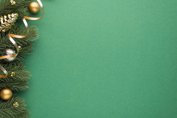 Foto von oben von Gold und Silber Weihnachtsbaumkugeln Spielzeugkegel kleine Glöckchen und Serpentin auf Kiefernzweigen auf isoliertem grünen Hintergrund mit Kopierraum - Foto, Bild