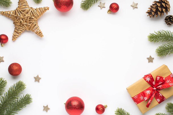 Top view φωτογραφία του πεύκου κλαδιά κόκκινο χριστουγεννιάτικο δέντρο μπάλες μπαστούνι κώνους αστέρι και κουτί δώρου με τόξο σε απομονωμένο λευκό φόντο με copyspace στη μέση - Φωτογραφία, εικόνα