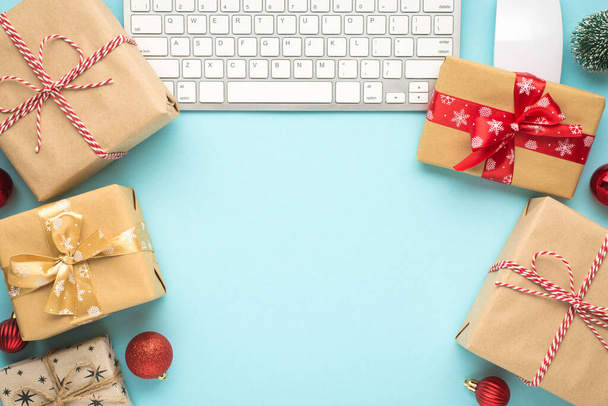 Vista superior de la foto de papel artesanal cajas de regalo teclado ordenador ratón pino juguete y bolas de árbol de Navidad rojo sobre fondo azul pastel aislado con espacio vacío - Foto, imagen