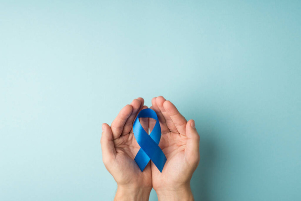 Première personne vue du dessus photo des mains de l'homme tenant un ruban bleu dans les paumes symbole de la sensibilisation au cancer de la prostate sur fond bleu pastel isolé avec copyspace - Photo, image