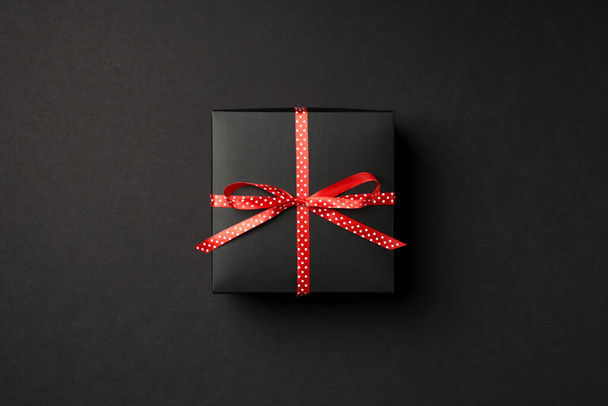 Фотографія зверху чорної подарункової коробки з червоним пунктирним стрічковим бантом на ізольованому чорному тлі
 - Фото, зображення