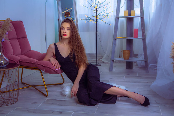 portrait of Glamour woman with red lips in black overalls sits on the floor at home - Фото, изображение