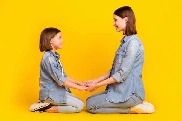 Photo of pretty charming siblings dressed denim shirts sitting floor holding arms smiling isolated yellow color background. - Foto, Imagen