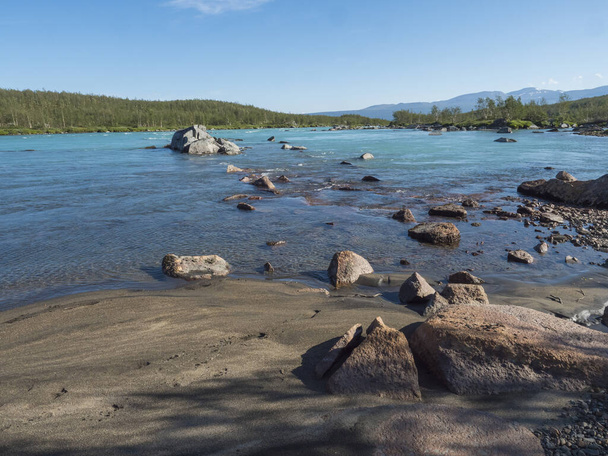 View of turquoise blue water of wild Vuojatadno river. Northern landscape in Swedish Lapland with birch tree forest and green mountains at Padjelantaleden hiking trail. Summer sunny day, blue sky - Photo, Image