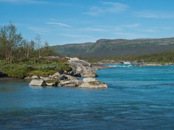 Blick auf das türkisblaue Wasser des wilden Flusses Vuojatadno. Nördliche Landschaft in Schwedisch Lappland mit Birkenwald und grünen Bergen am Padjelantaleden-Wanderweg. Sommer sonniger Tag, blauer Himmel - Foto, Bild