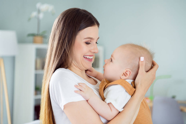 Photo of glad cheerful charming mother lady carry embrace little baby boy son wear white t-shirt home indoors. - Foto, Imagem