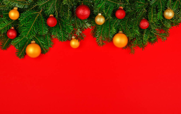 Close up fresh green spruce Christmas tree branches decorated with cones, golden balls and baubles, over red background with copy space - Fotografie, Obrázek