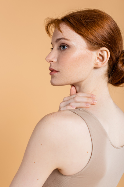Pretty red haired woman touching neck and looking away isolated on beige  - Foto, Imagen