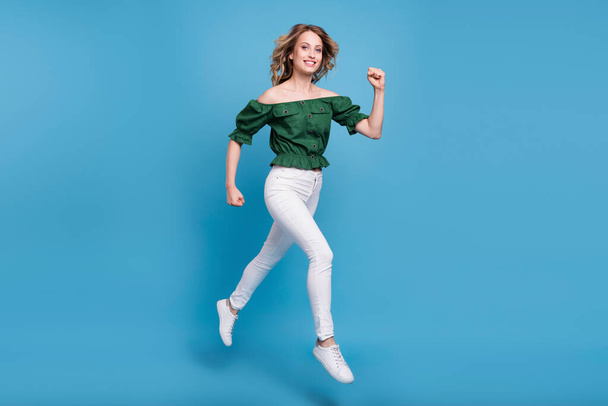 Photo of charming sporty lady skok bieg zużycie niedźwiedź ramiona zielony bluzka spodnie buty odizolowany niebieski kolor tło. - Zdjęcie, obraz