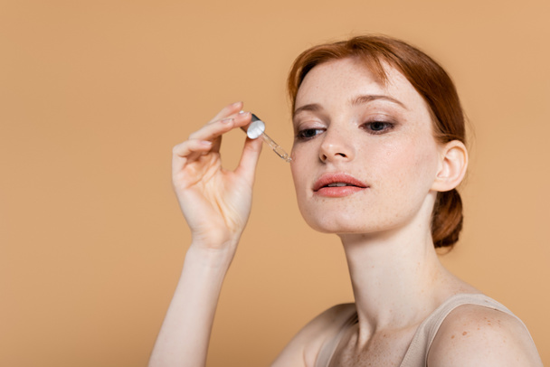 Pretty woman with clean skin applying cosmetic serum isolated on beige  - Фото, зображення