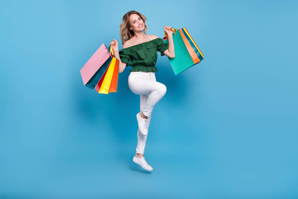 Photo of shopaholic lady jump carry bags wear bear shoulders green blouse pants shoes isolated blue color background. - Φωτογραφία, εικόνα