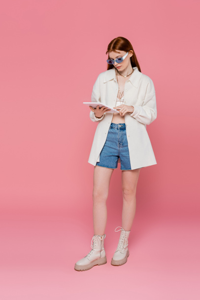 Longitud completa de la joven mujer con estilo utilizando tableta digital sobre fondo rosa - Foto, imagen