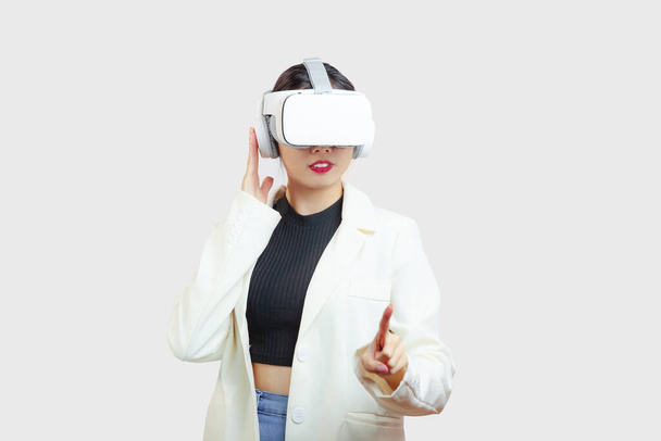 Metaverse, asian woman in white jacket wearing virtual reality glasses pointing and touching on the white background. - Фото, зображення