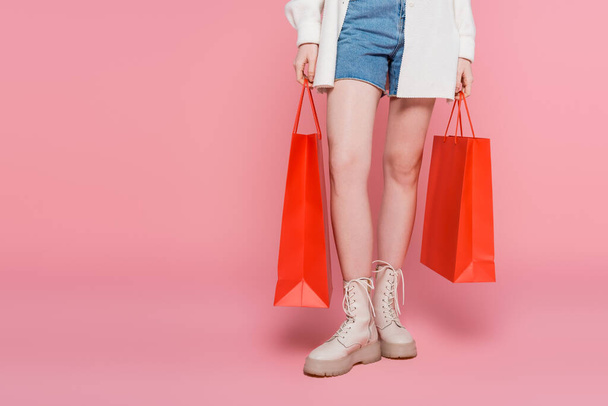 Cropped view of woman in denim shorts holding shopping bags on pink background - Φωτογραφία, εικόνα