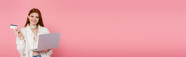 Mulher bonita e elegante segurando cartão de crédito e laptop isolado em rosa, banner - Foto, Imagem