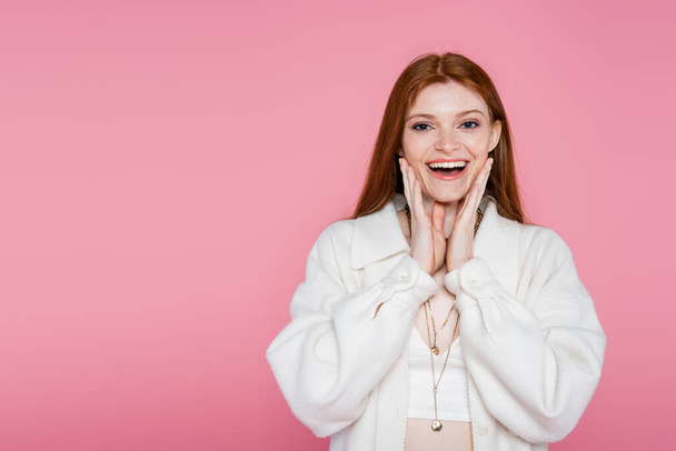 Excited redhead woman in jacket looking at camera isolated on pink  - Foto, imagen