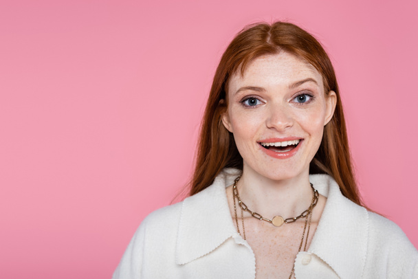 Positive freckled woman in jacket and necklaces looking at camera isolated on pink  - Foto, afbeelding