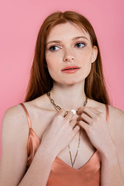 Portrait of redhead woman in dress touching necklace isolated on pink  - Foto, Imagem