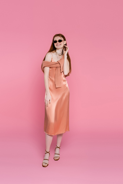 Full length of smiling woman in dress and sunglasses posing on pink background  - Foto, immagini