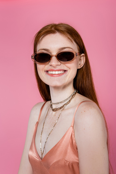 Portrait of stylish freckled woman in sunglasses isolated on pink  - Фото, изображение