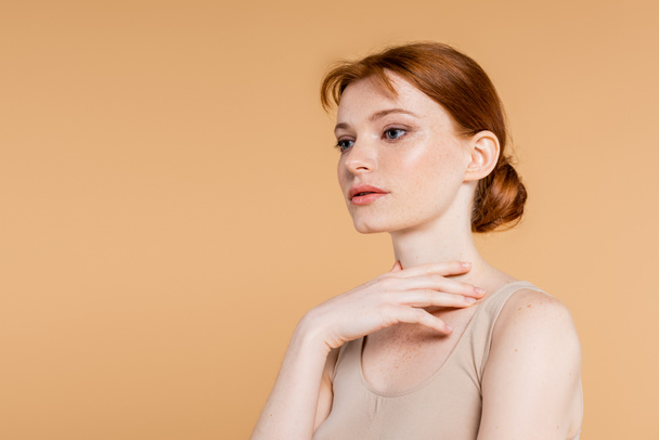 Pretty redhead woman touching neck isolated on beige  - Foto, imagen