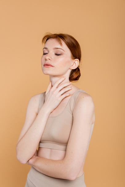 Pretty young woman in top touching neck isolated on beige  - Photo, Image