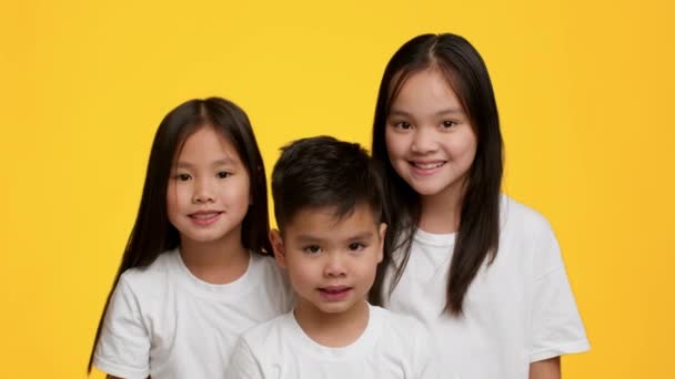 İki mutlu Japon kız kardeş ve küçük kardeş pozu, sarı arka plan - Video, Çekim