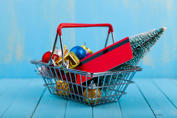 Shopping basket with Christmas gifts, decor and credit card on a blue wooden background. Christmas sale. - Fotografie, Obrázek