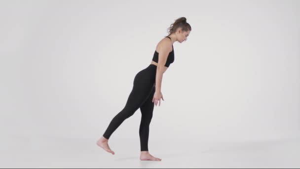 Posturas básicas de yoga. Retrato de vista lateral de una joven mujer flexible de pie sobre una pierna e inclinada hacia adelante, levantando la pierna - Metraje, vídeo