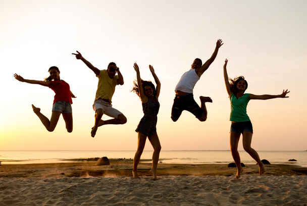 lachende vrienden dansen en springen op strand - Foto, afbeelding