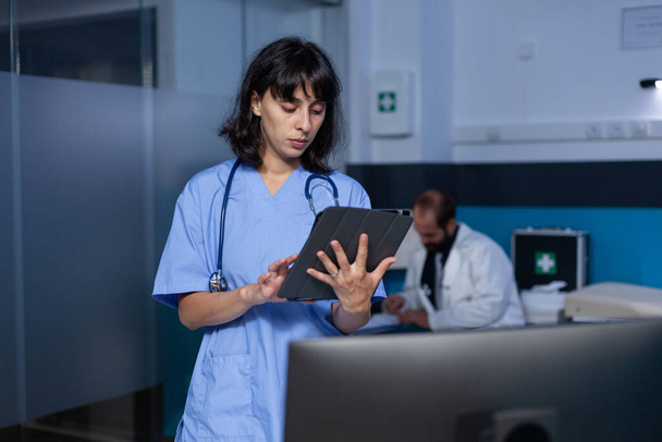 Mulher enfermeira olhando para tablet digital trabalhando até tarde da noite - Foto, Imagem