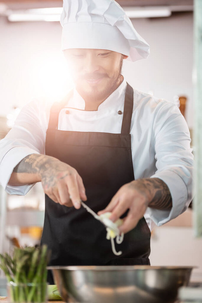 Souriant asiatique chef tenant poireau tranché près bol dans la cuisine  - Photo, image